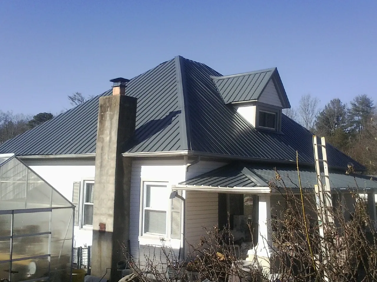 Dark blue standing seam metal roof on a white farmhouse with dormer — Slate & Tile Roof Repair by Roofing Brothers in Grand Ronde