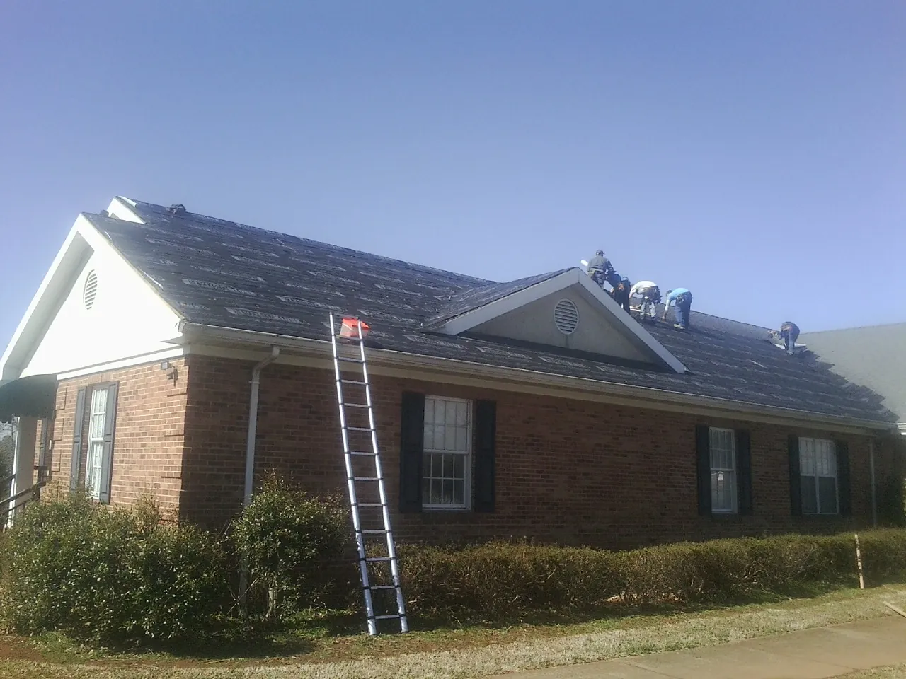 Crew tearing shingles off a brick ranch roof with a ladder set — Emergency Roof Repair work by our crew in Grand Ronde