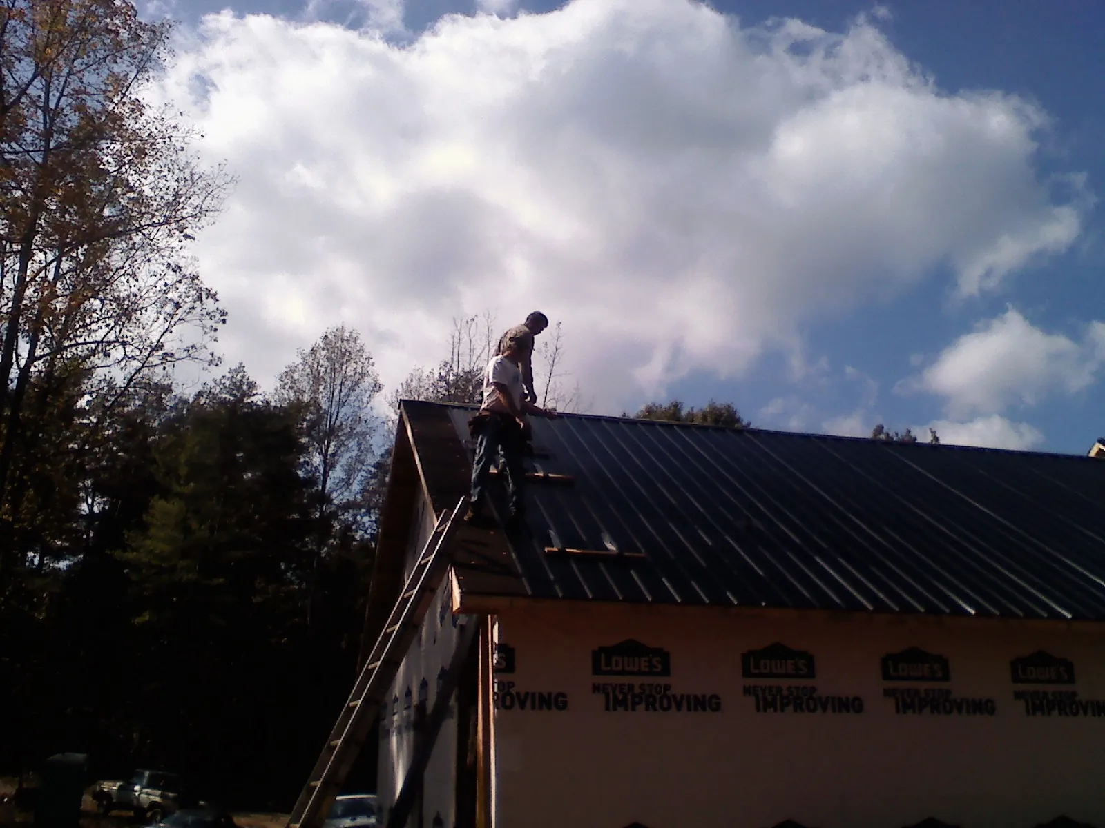 Roofer fastening dark metal panels high against a cloudy sky, from a Roof Inspection job in Grand Ronde