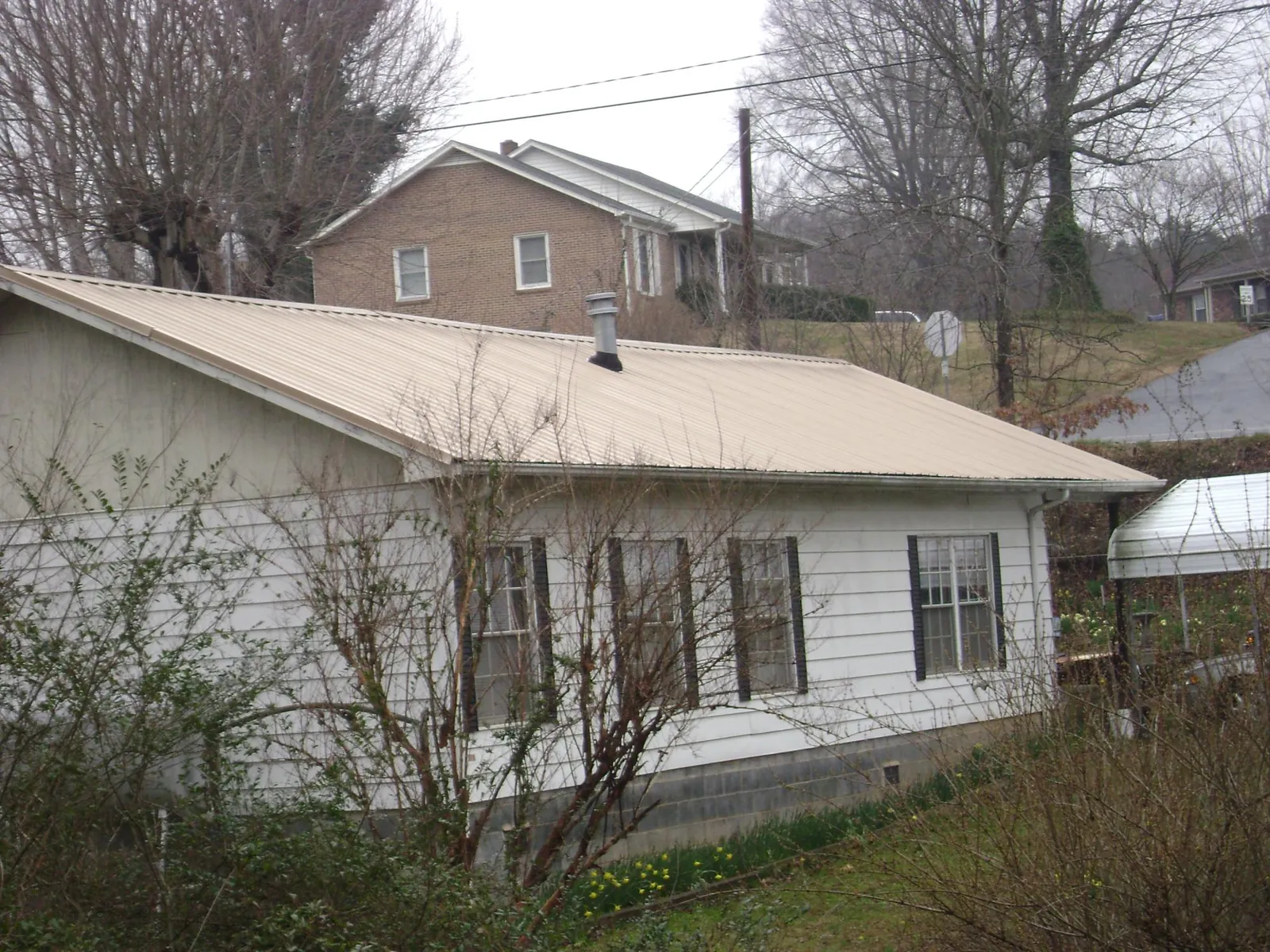 Tan metal roof on a white sided house set into a hillside — Commercial Roofing by Roofing Brothers in Grand Ronde